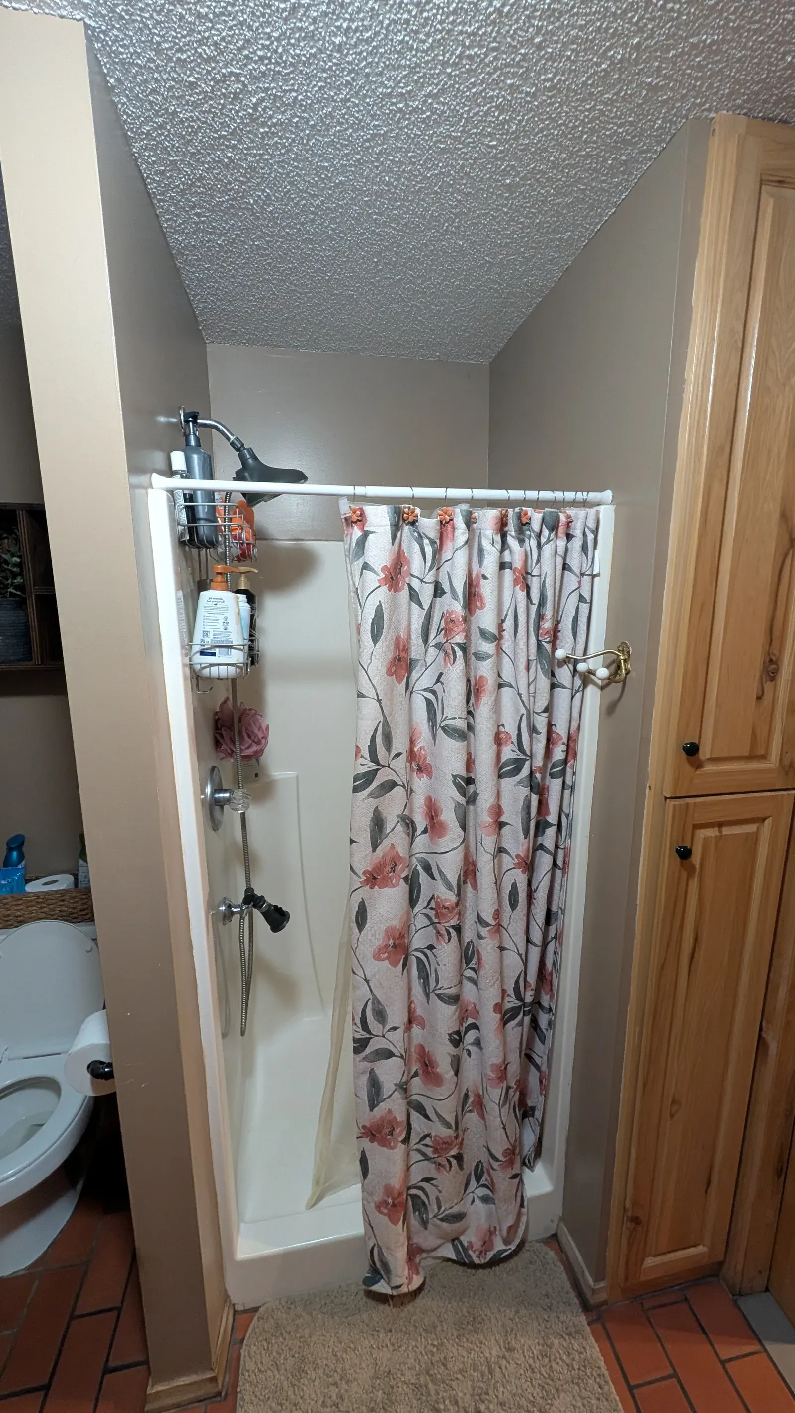 Original bathroom with cramped shower stall and floral curtain