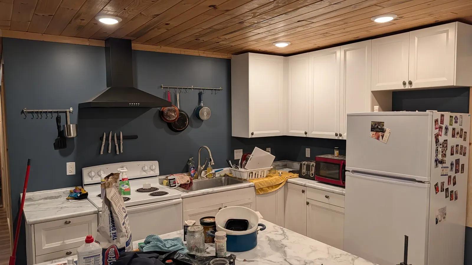 Updated kitchen with blue accent wall, white cabinets, range hood, and pine ceiling