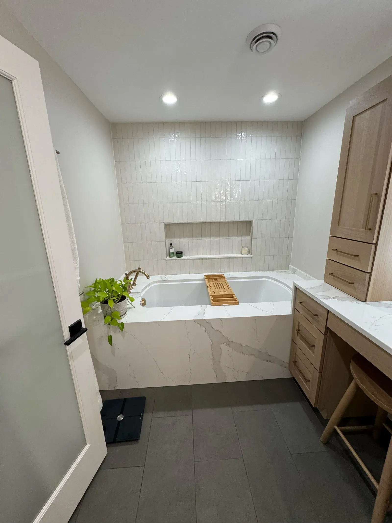 New soaking tub with quartz-clad surround, vertical tile accent wall, and built-in niche