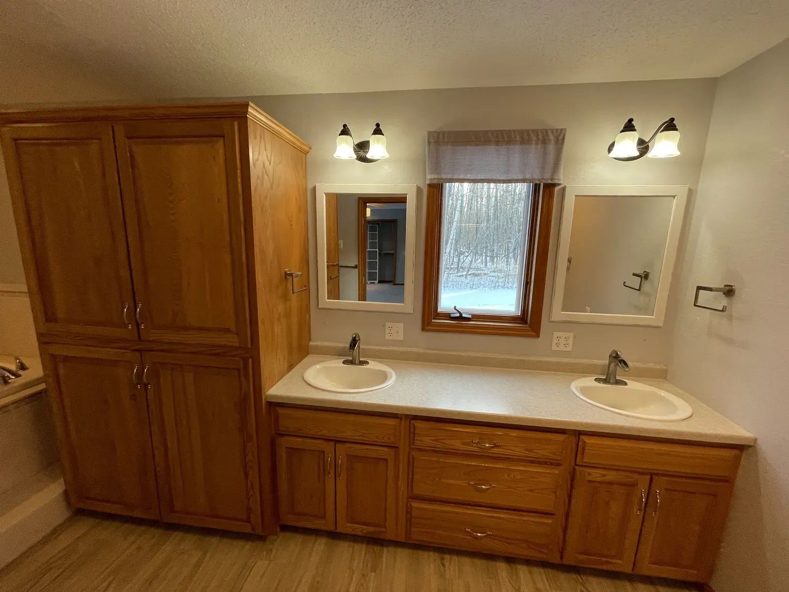 Old double vanity with oak cabinets and dated light fixtures
