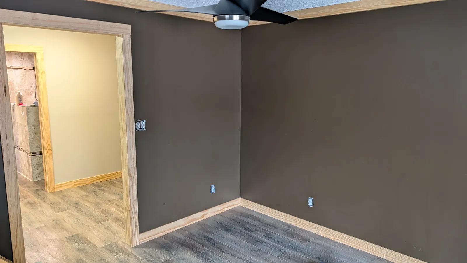 Completed master bedroom with smooth walls, dark accent paint, LVP flooring, and ceiling fan